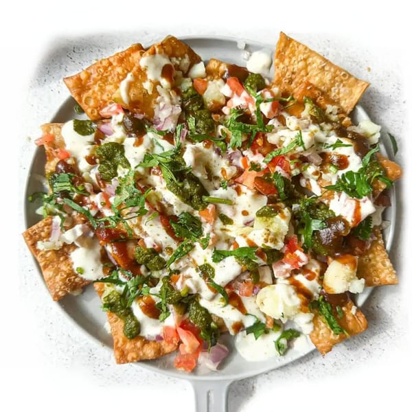 A close-up of Pakistani chaat with crispy flatbread, yogurt, chutneys, and fresh herbs.