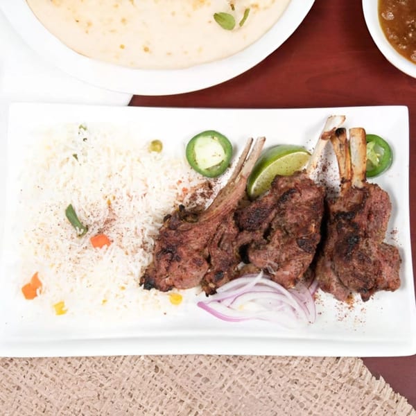 Mehran Restaurant's lamb chops with rice, lime, jalapenos, and red onions on a white plate.