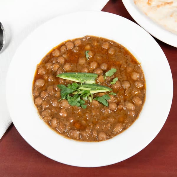A white bowl of Pakistani chana masala, garnished with green chilies and cilantro, on a red table.