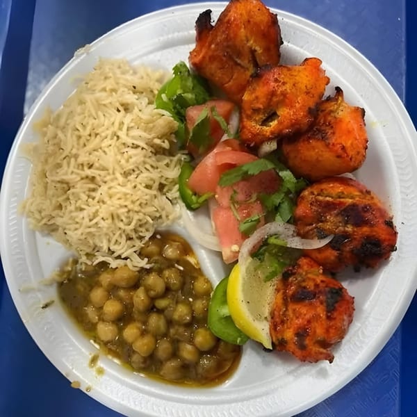 Pakistani chicken tikka with rice, chickpea curry, and salad on a white plate.