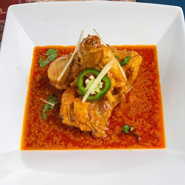 Pakistani chicken karahi in a rich orange sauce, garnished with cilantro, ginger, and a jalapeño slice.