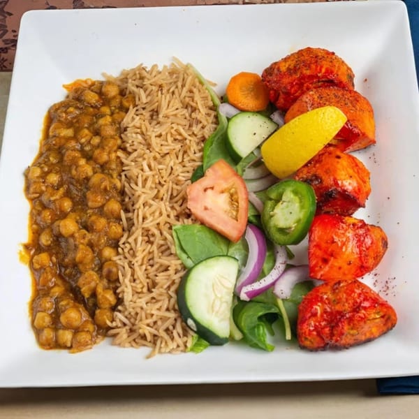 Mehran Restaurant's chicken tikka, chana masala, rice, and fresh salad with lemon on a white plate.